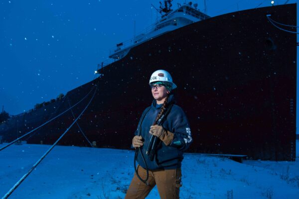 Woman boilermaker stands in front of laker freighter